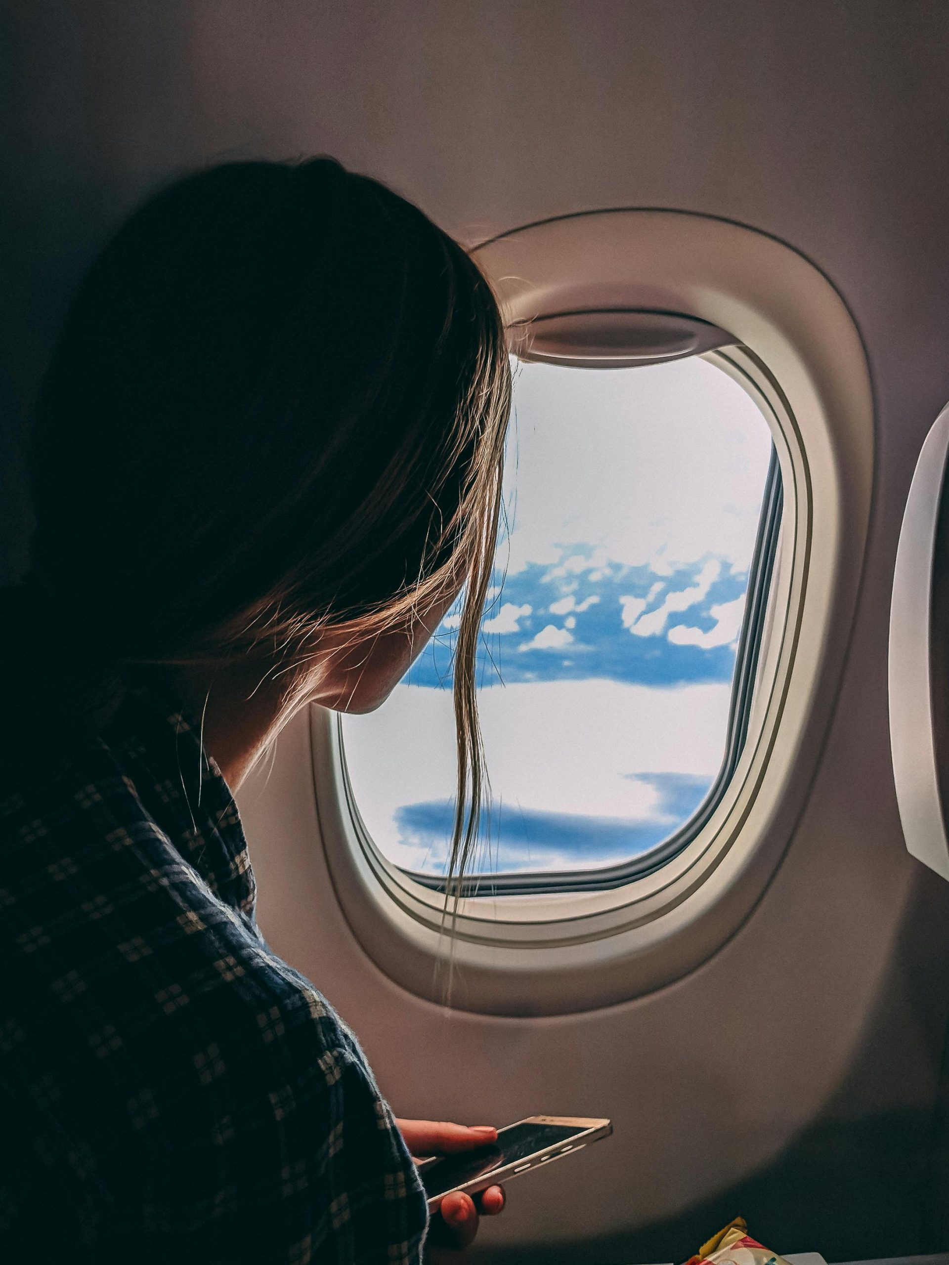 pexels-photo-2033343-2033343 A woman looks out an airplane window, capturing a serene view of clouds and sky during a flight.